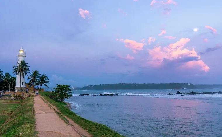 The lighthouse and shoreline path at Galle under a pink evening sky