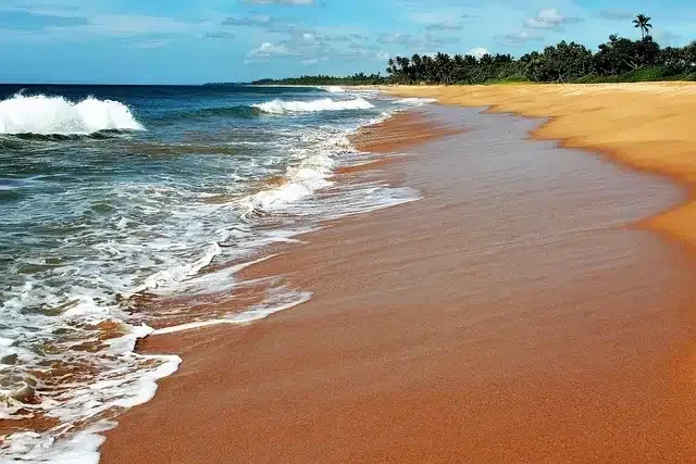 Surf breaking along a wide golden beach at Bentota